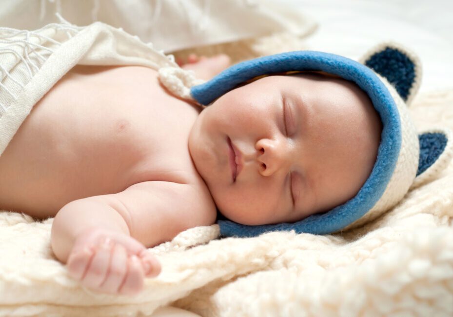Sleeping baby wearing blue bear hat.